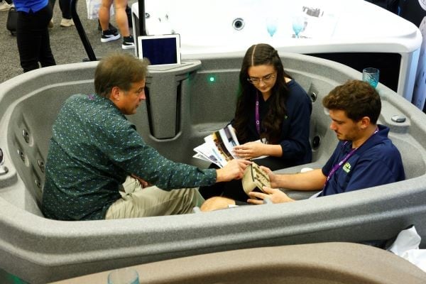 Pool professionals sitting in a hot tub spa at an exhibitor booth at International Pool Spa Patio Expo